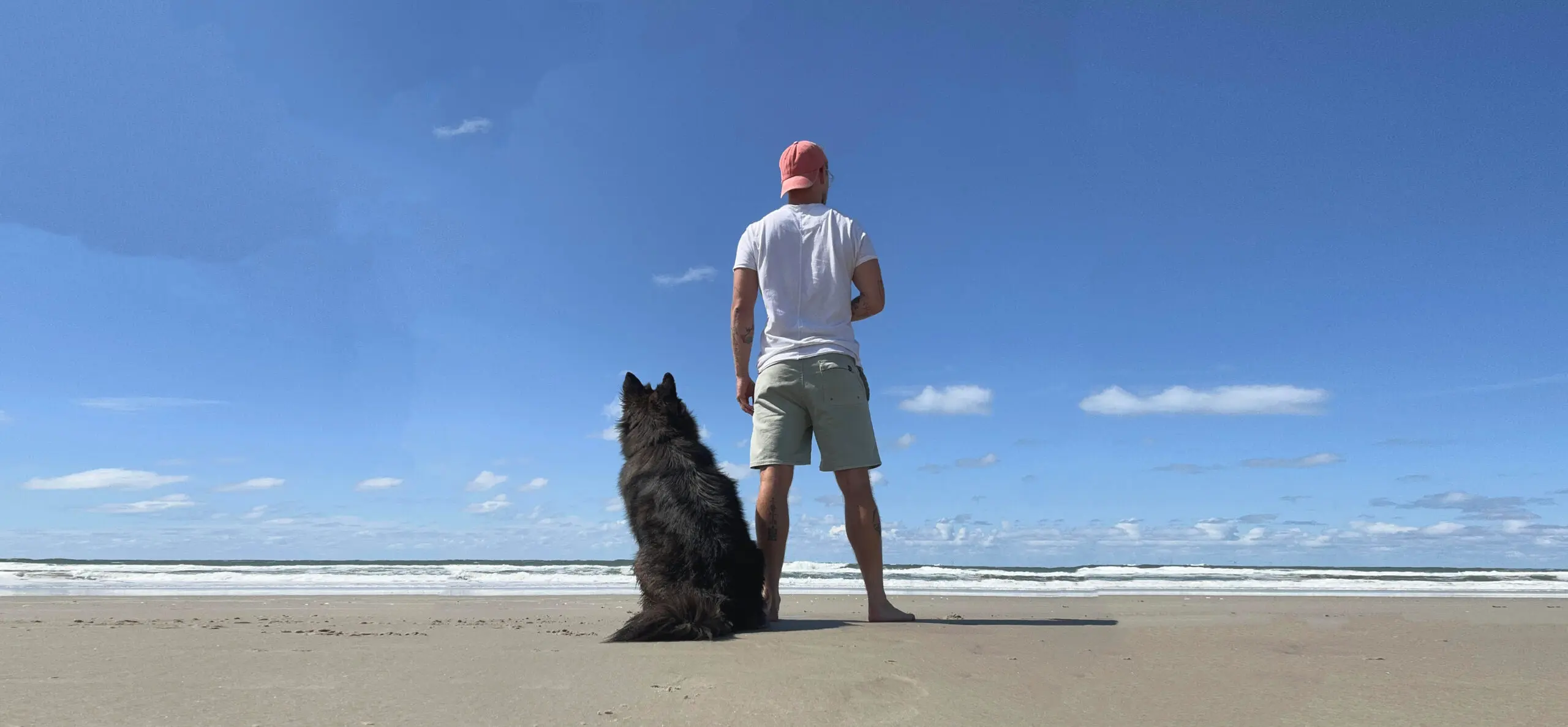 Patrick und Balou stehen nebeneinander am Strand und schauen gemeinsam aufs Meer